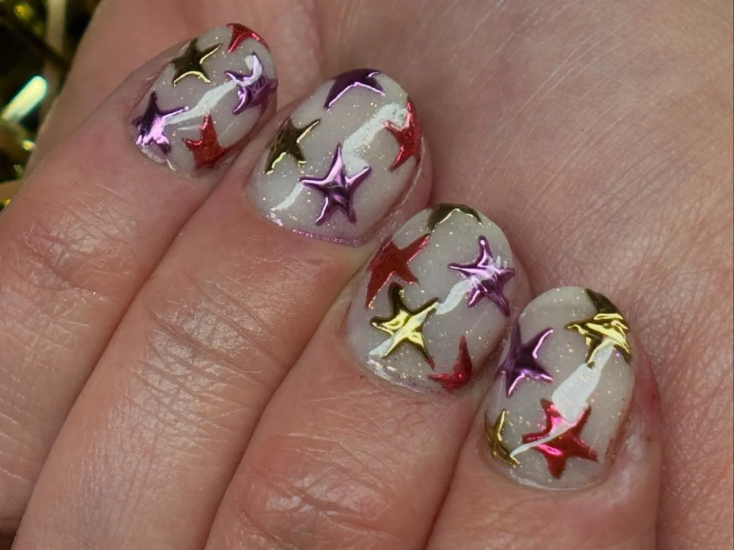 Close-up of fingernails with glittery white polish and multicolored star-shaped nail art in purple, red, gold, and white.