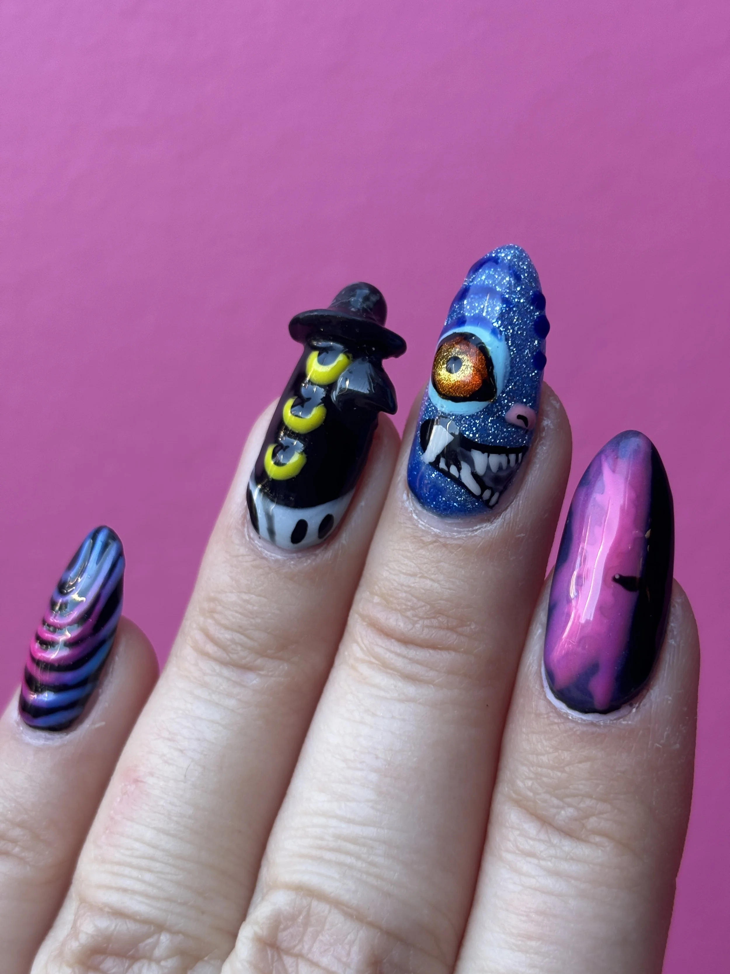 Close-up of hand with decorated nails featuring a witch, eyeball, and rainbow designs against a pink background.