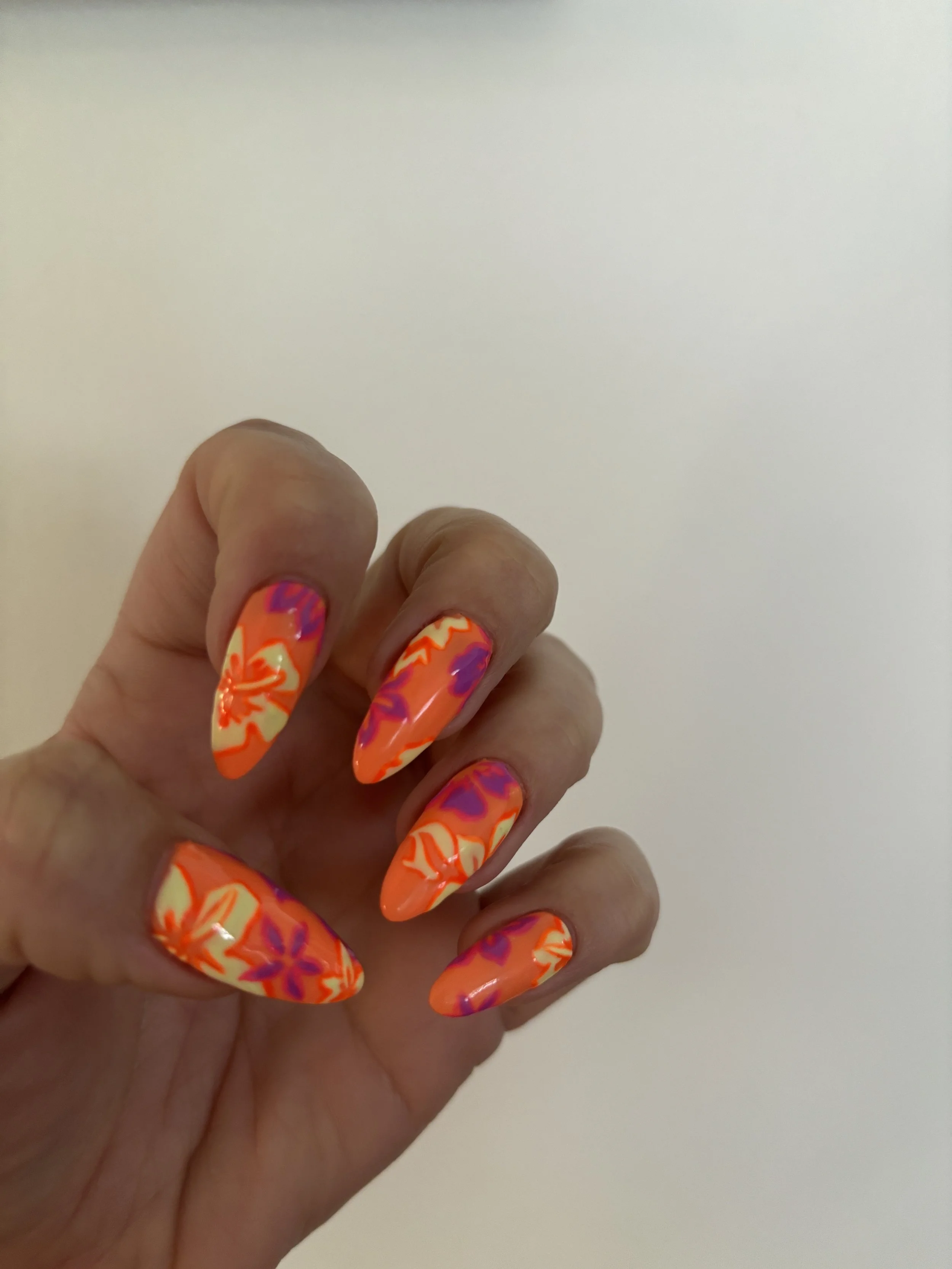 A hand with brightly colored, floral-patterned, long acrylic nails.