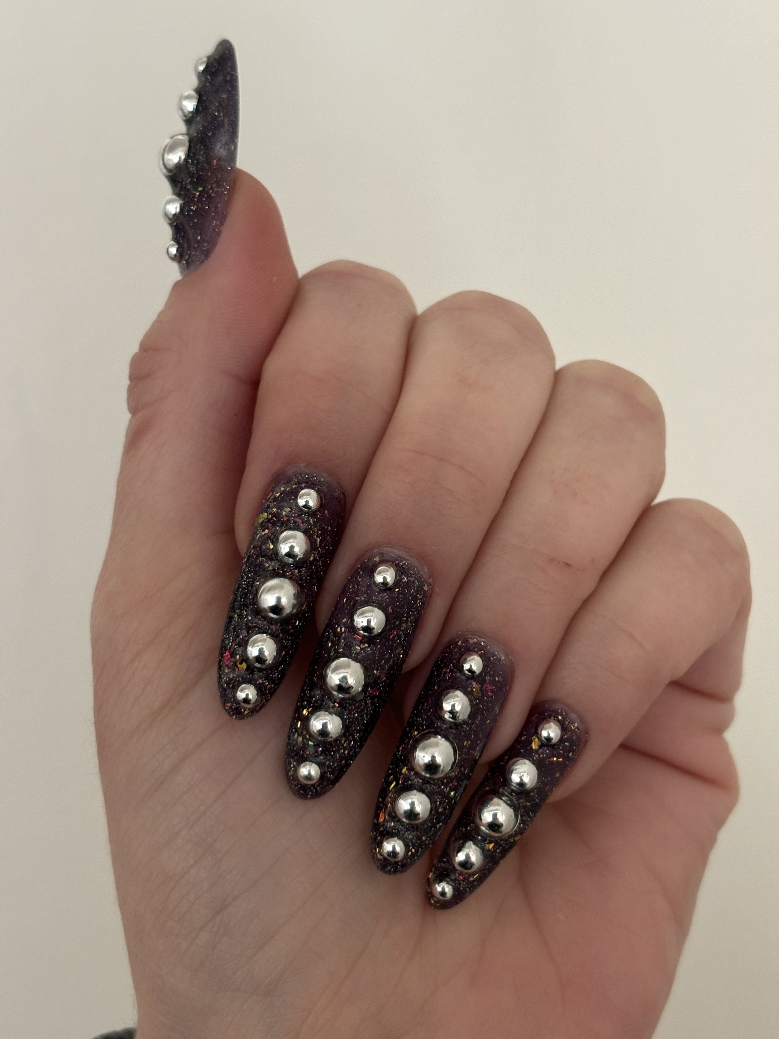 Close-up of a hand with long, dark, glittery nails decorated with silver studs.