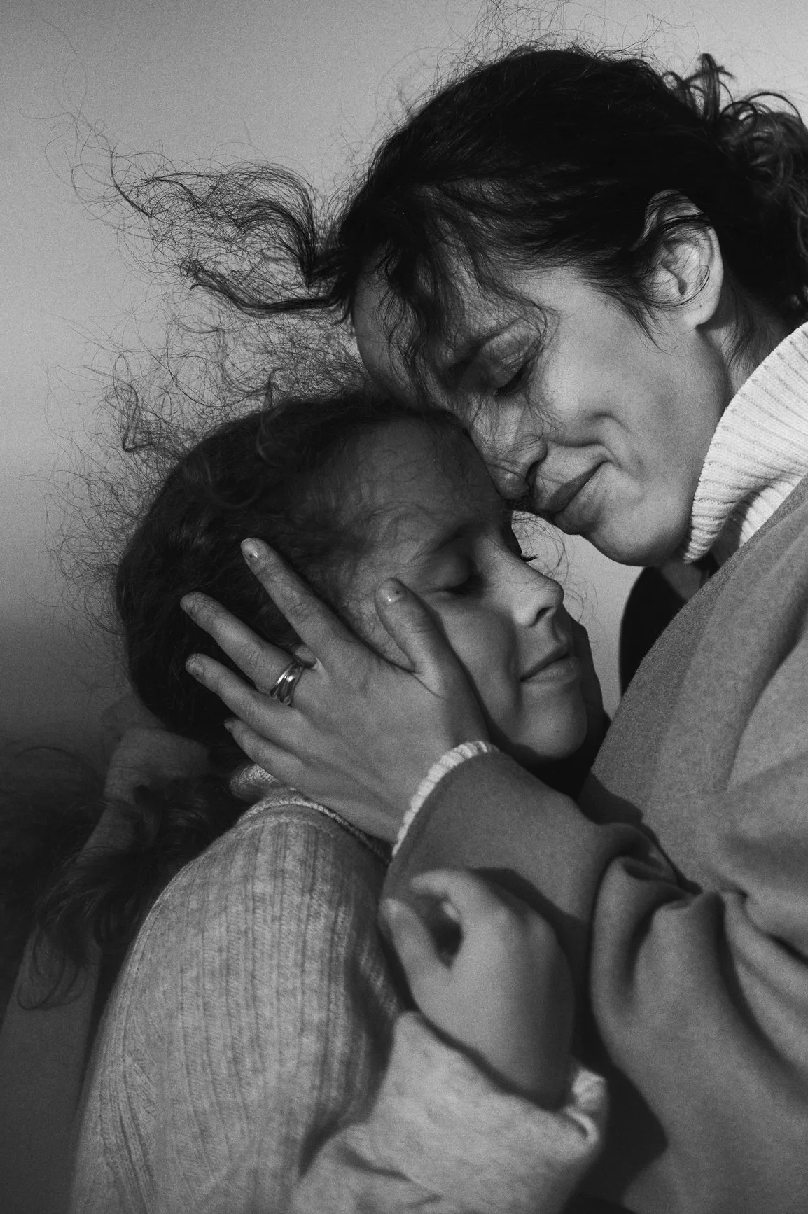 A black-and-white photograph of a woman and a girl sharing an emotional embrace, with their eyes closed and foreheads touching.