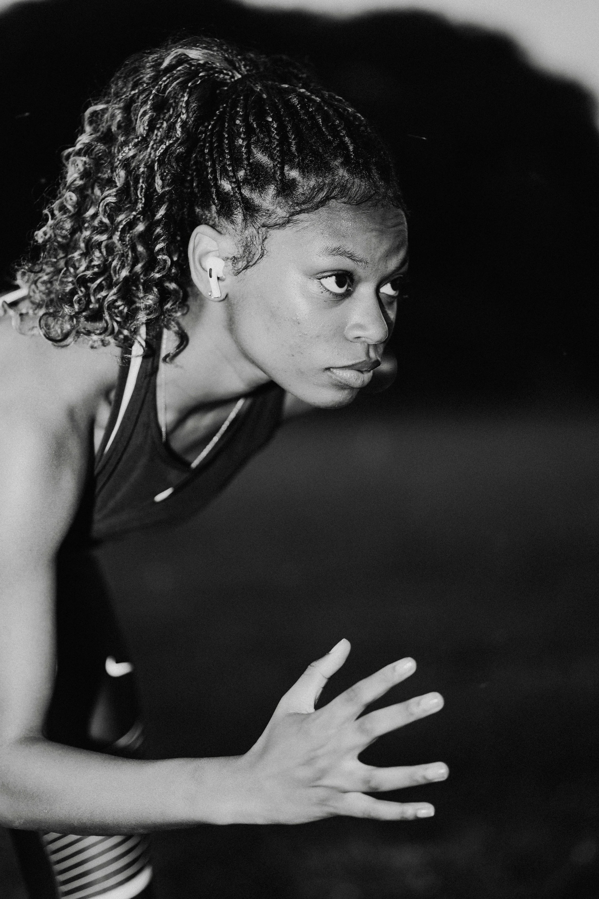A woman with braided and curly hair in athletic gear, looking focused and ready to run, with earphones in her ears, in black and white.
