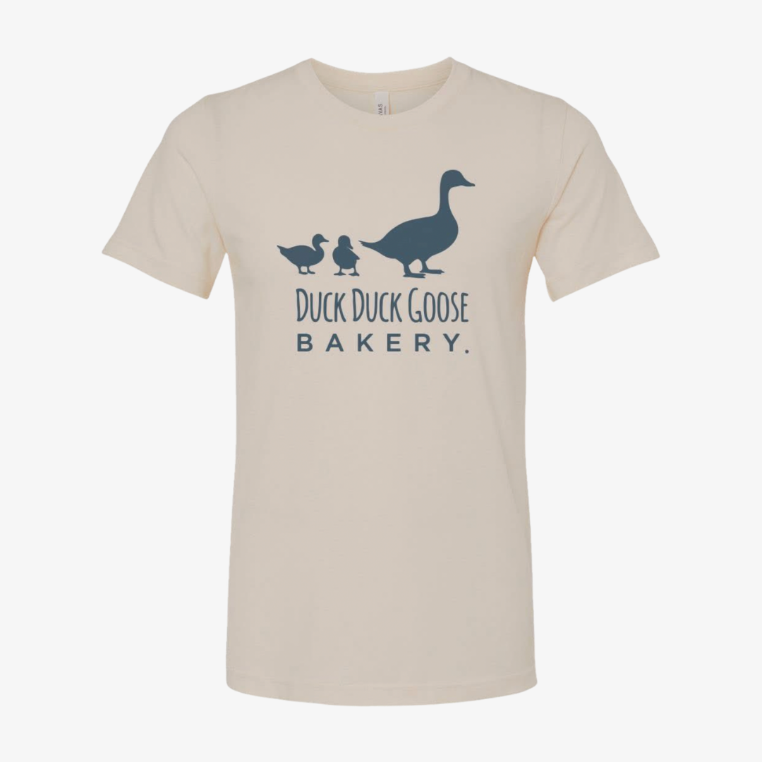 Duck Duck Goose Bakery tshirt with logo in middle of tan t-shirt.