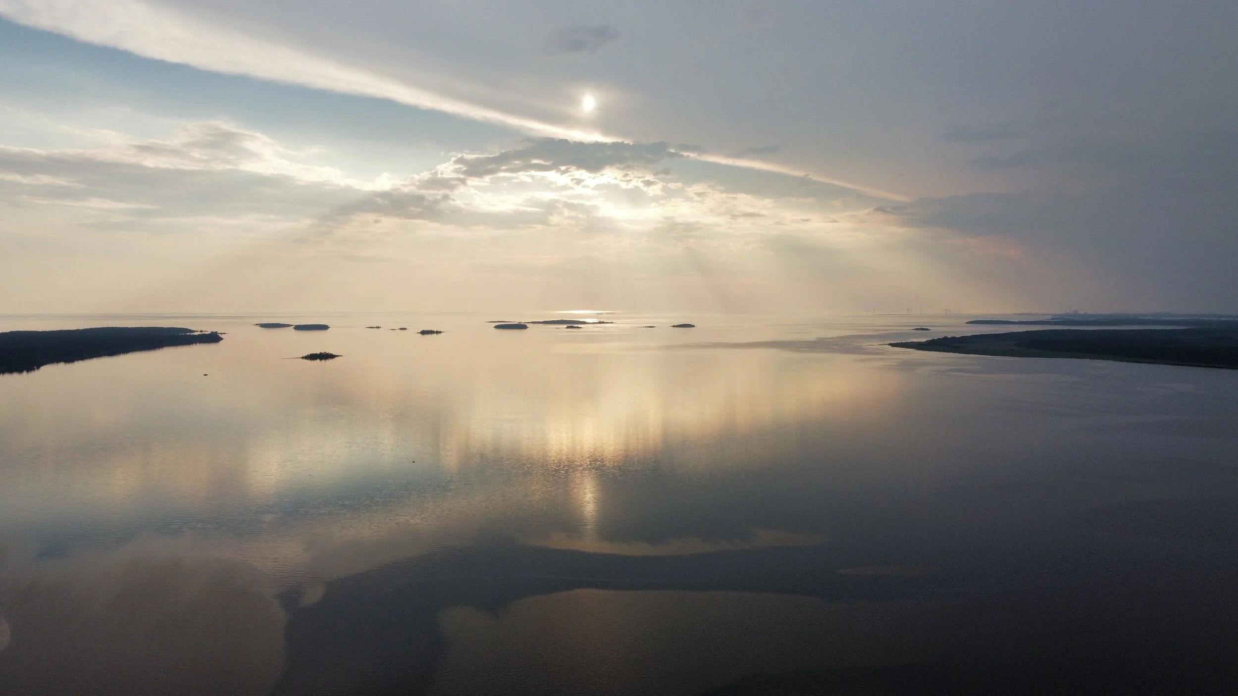 A vast body of water reflecting the sky and clouds, with small islands scattered across the horizon under a partly cloudy sky.