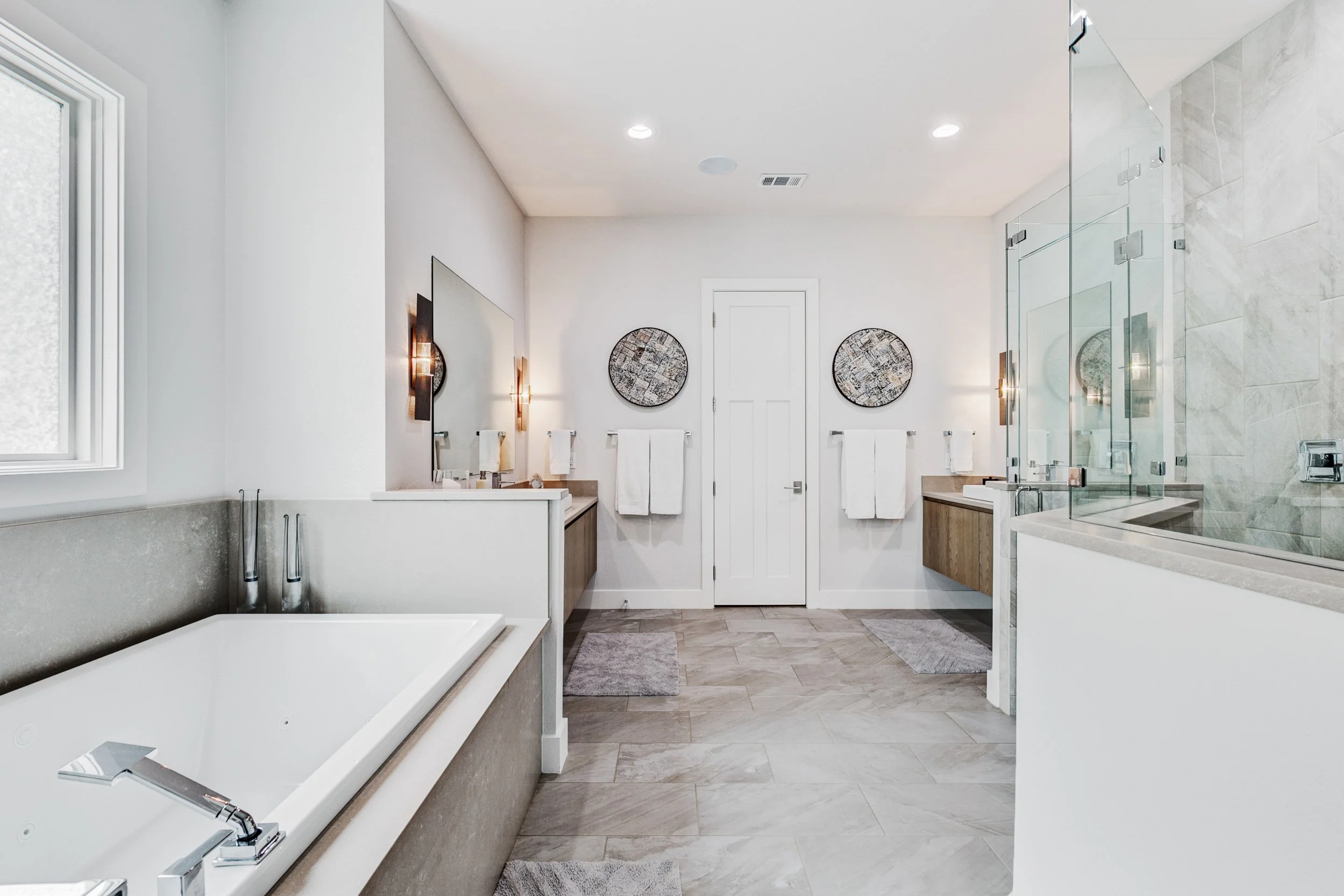 Modern bathroom with bathtub, double sinks, large mirror, wall art, towels, and a glass-enclosed shower.