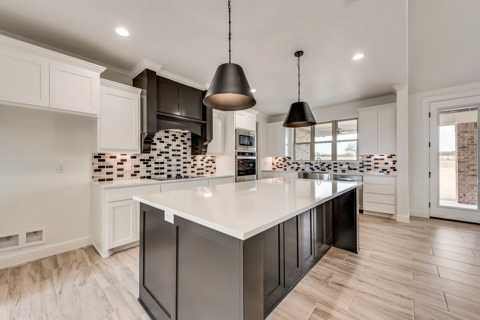 Modern kitchen with black and white cabinets, a large central island, pendant lights, and a mosaic tile backsplash.