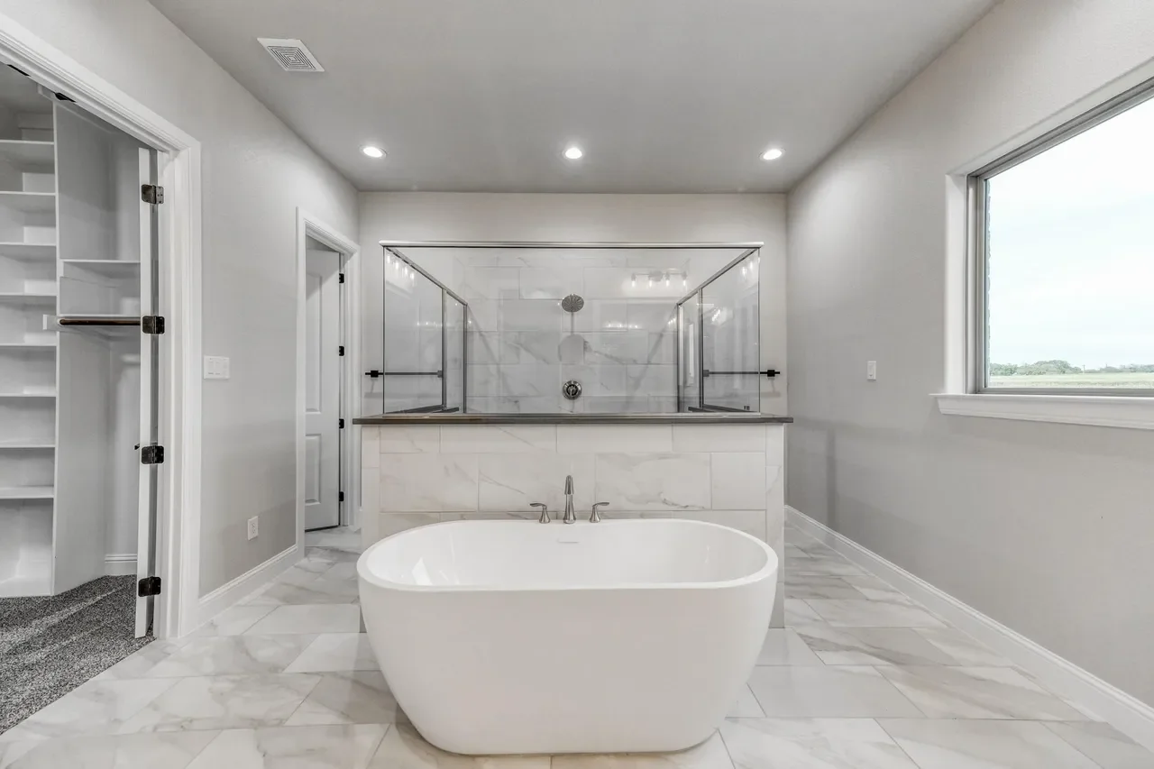 Modern bathroom with a freestanding bathtub, marble flooring, and a large window. A walk-in shower with glass enclosure is in the background.