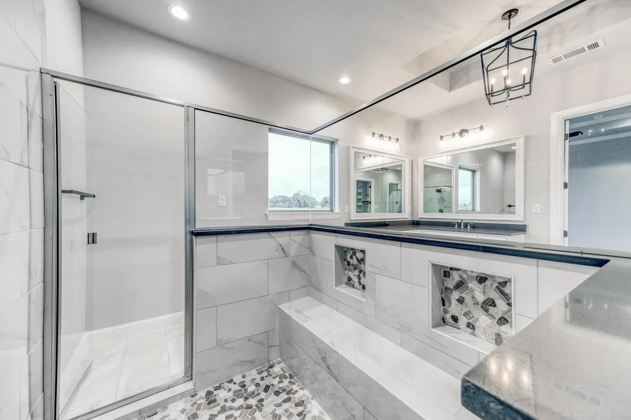 Modern bathroom with a glass-enclosed shower, large mirror, windows, and decorative tiled niches.