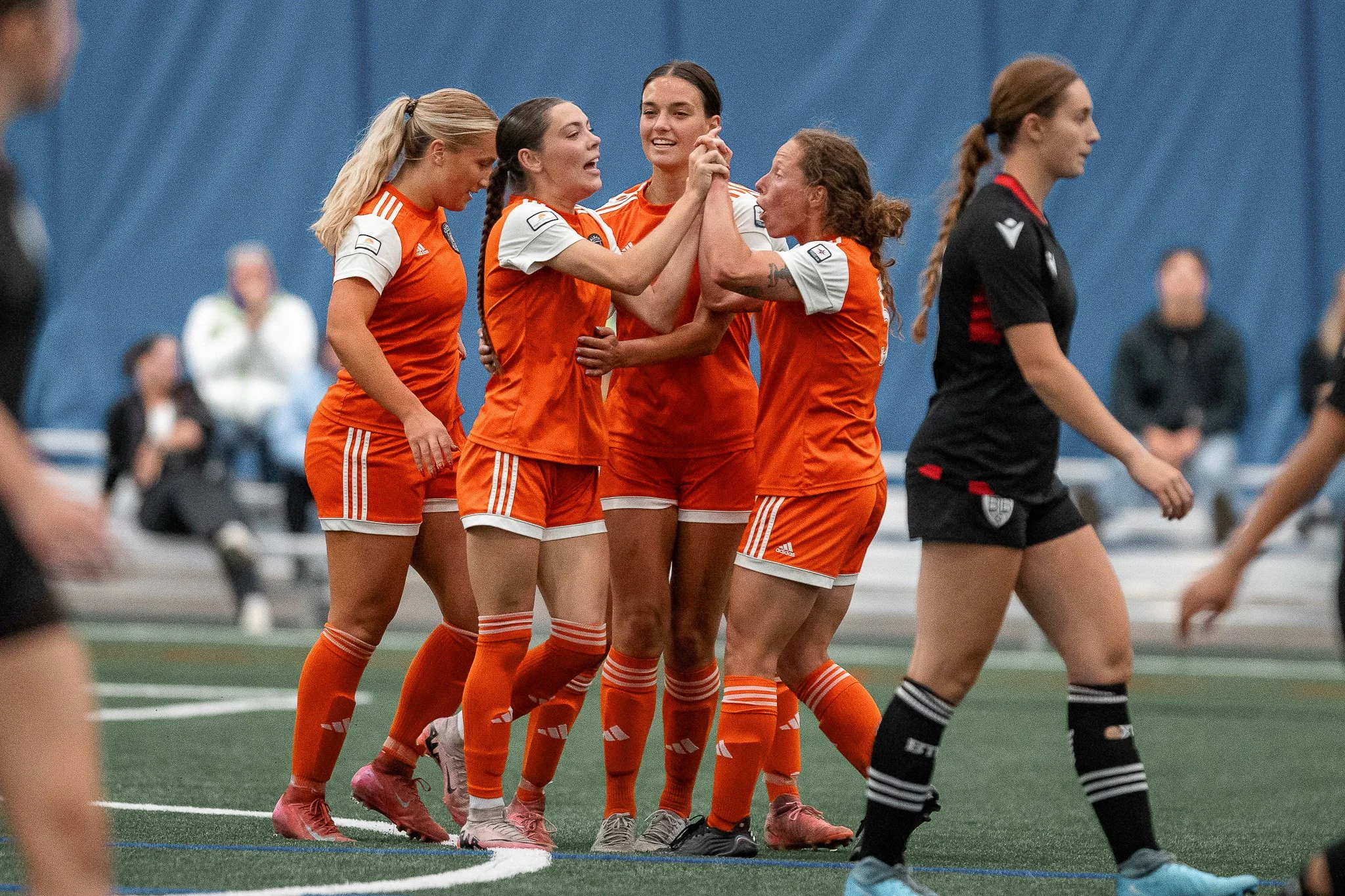 Soccer players in orange and black uniforms celebrating on the field during a match.