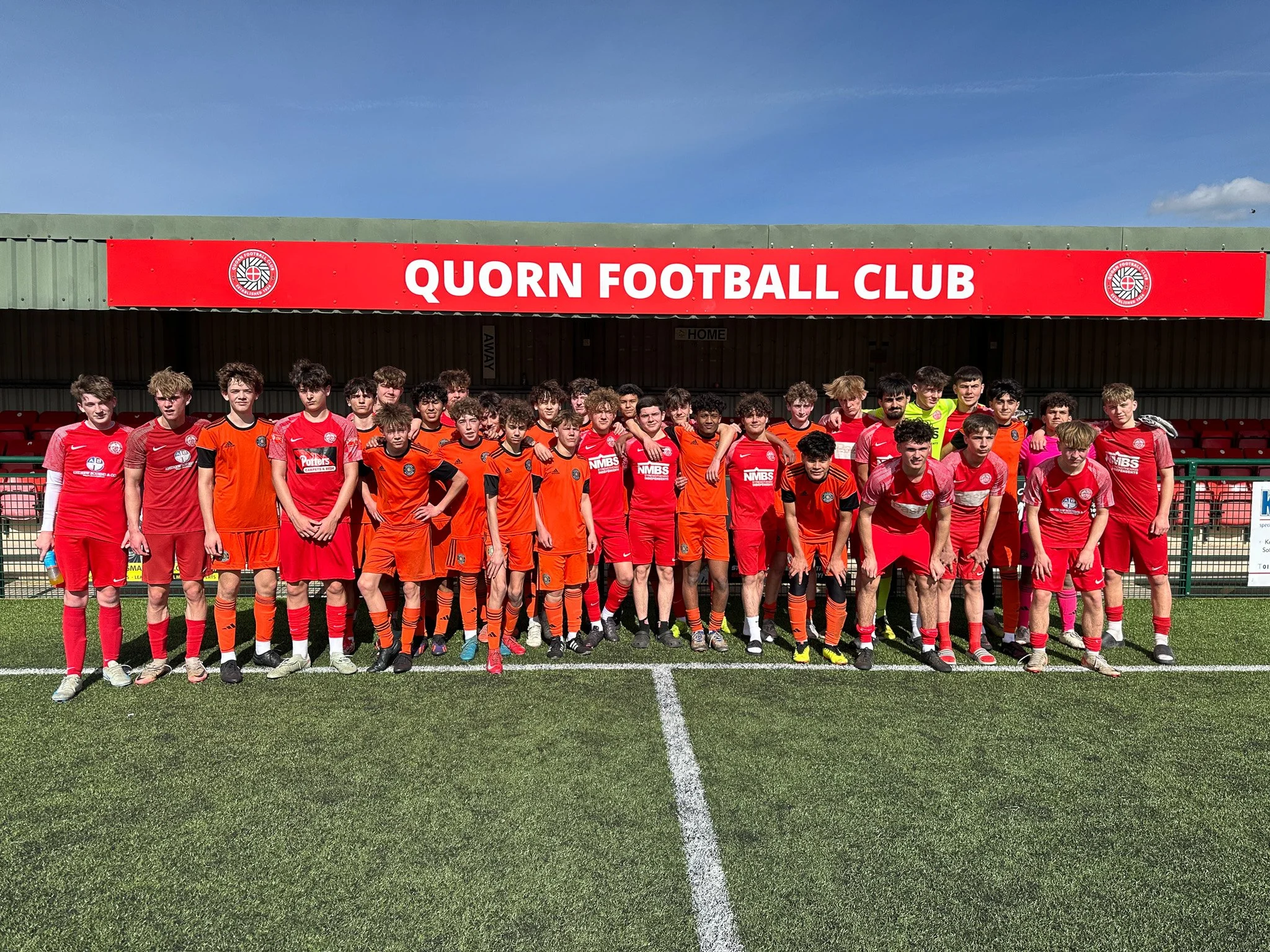 Group of young soccer players posing on a field with a banner reading 'Quorn Football Club' in the background.