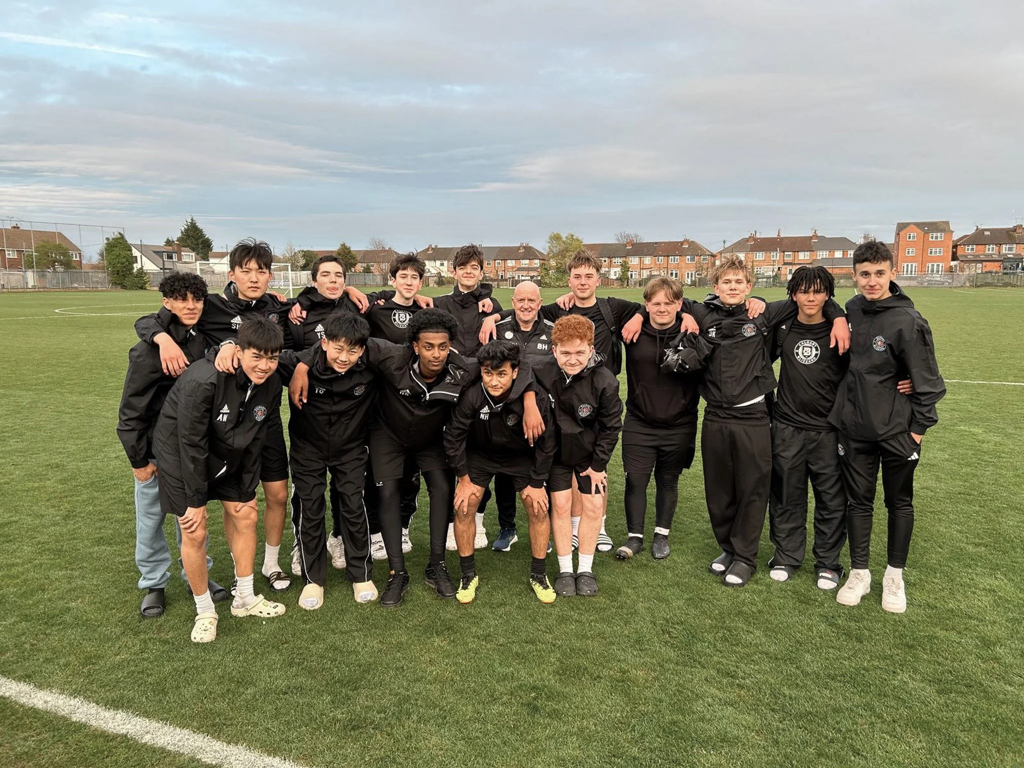 Young male soccer team with coach on a grass field, all wearing black jackets, standing together after a game.
