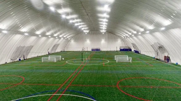 Indoor soccer field with multiple goals and colorful lines, inside a large, white, dome-shaped structure.
