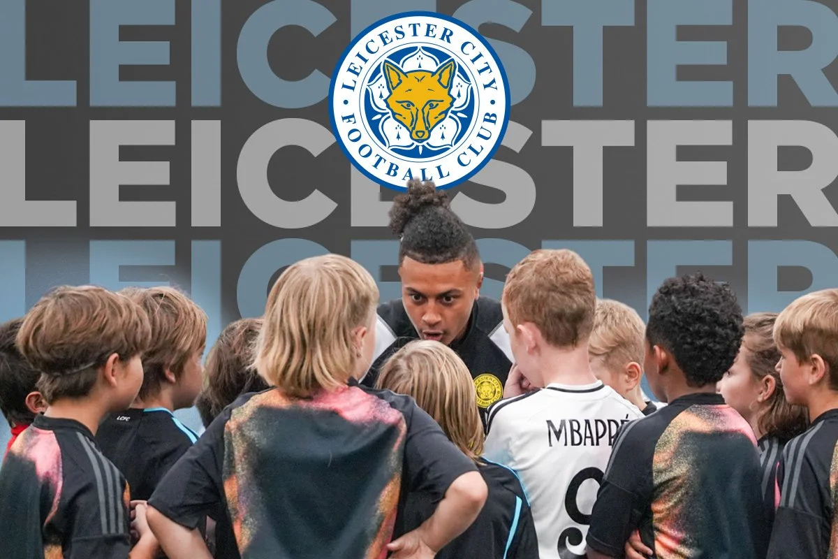 Group of young soccer players in black and colorful jerseys listening to coach during a team talk. Background features Leicester City Football Club logo, text 'LEICESTER' repeated in gray, and an announcement for Calgary Blizzard soccer registration opening in July 2026.
