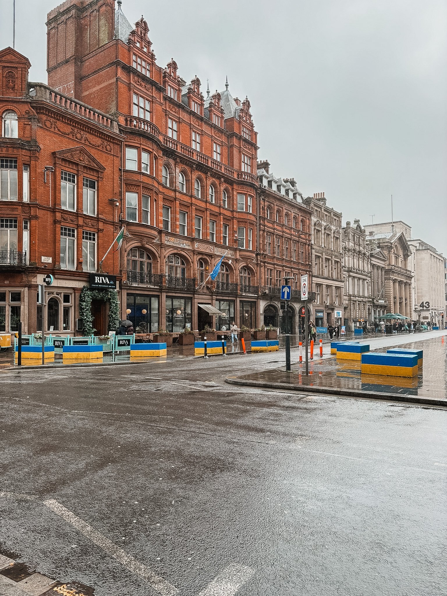 City street scene with old brick buildings, some shops, wet pavement, and a cloudy sky.