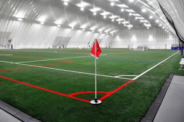 Inside an inflatable indoor soccer field with artificial turf, corner flag in foreground, and goalposts in the background.