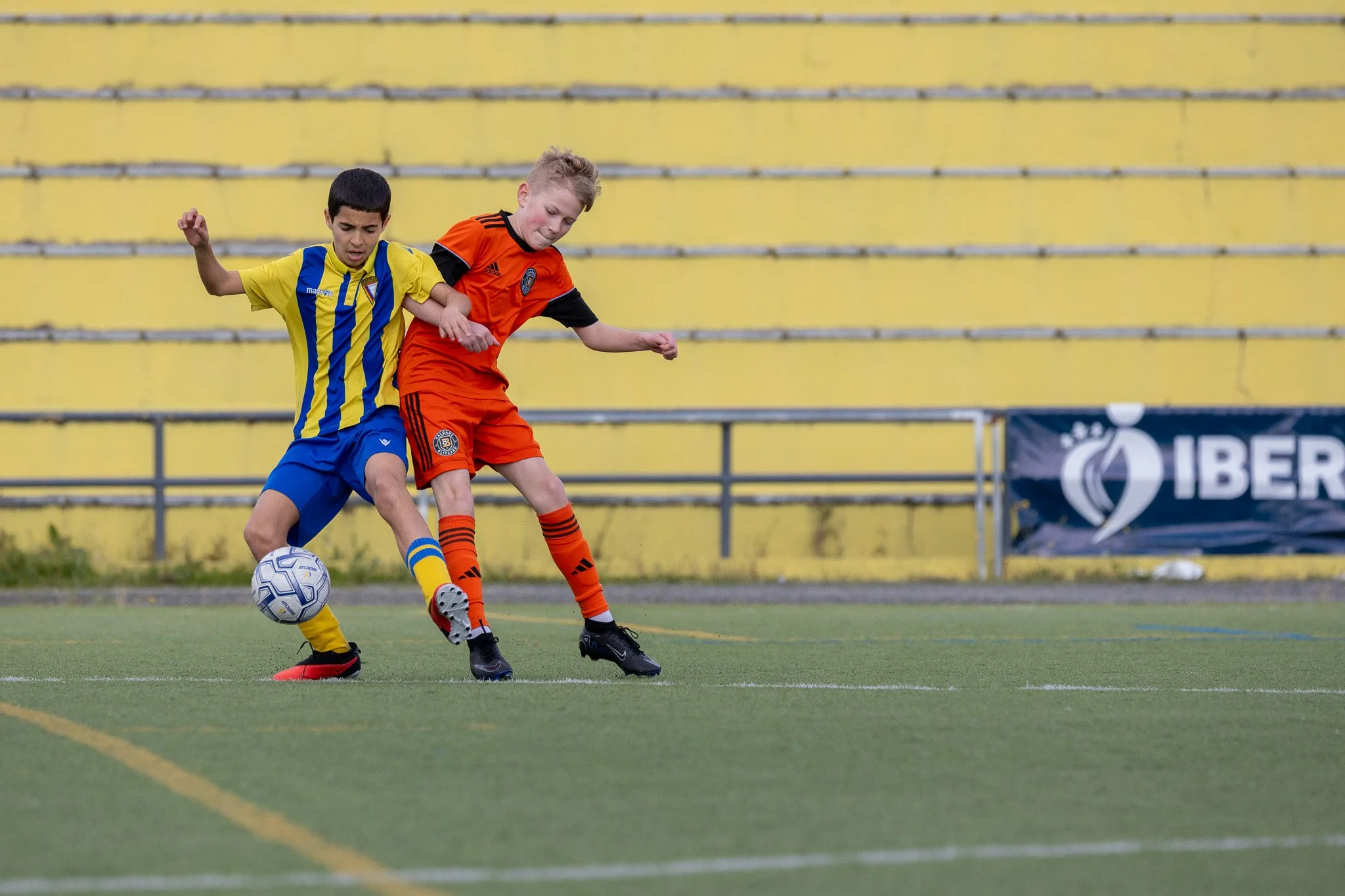 Two young boys playing soccer on a field, competing for the ball.
