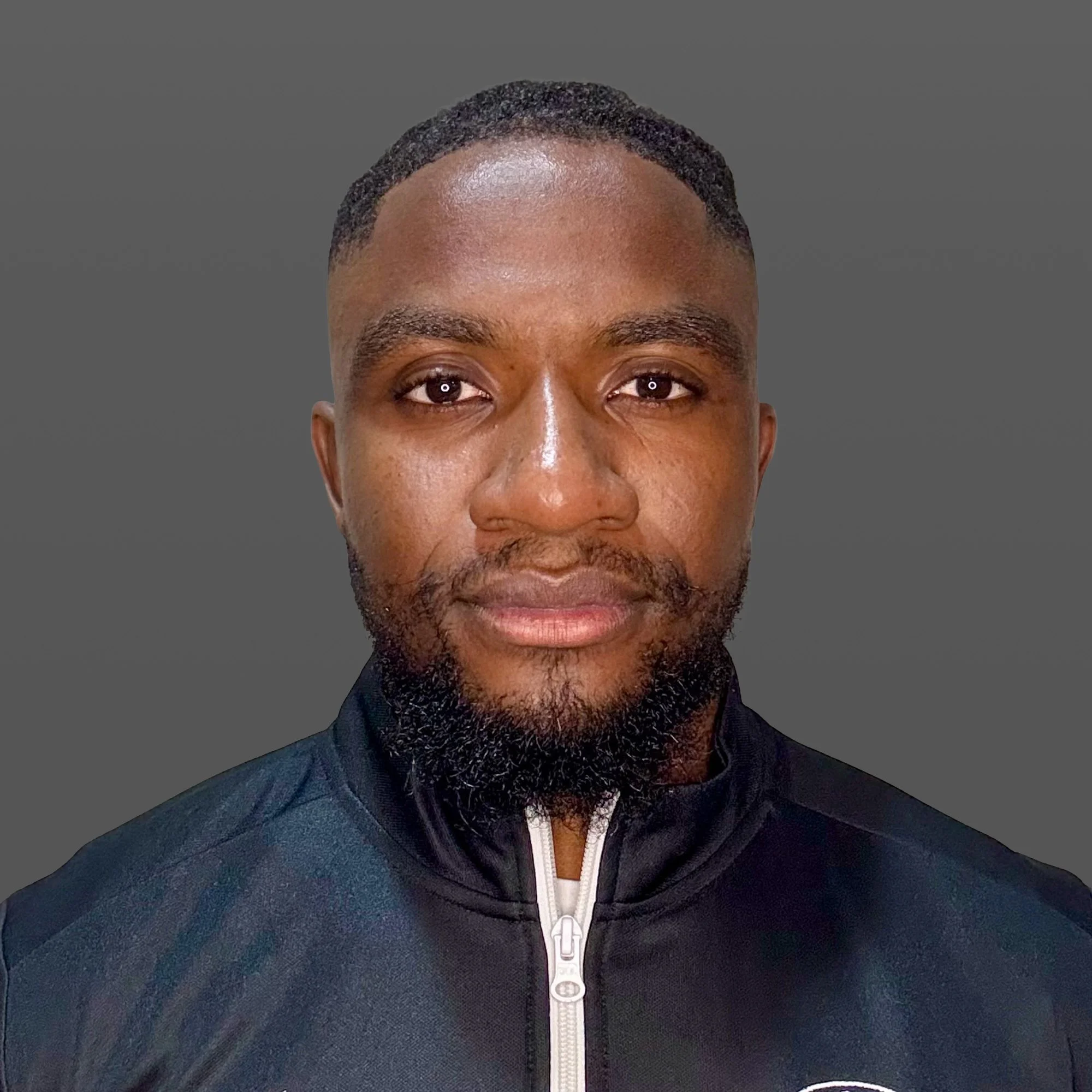A man with a short haircut and beard wearing a black Adidas sports jacket with a logo matching the Hungarian flag colors, standing outdoors at night on a sports field.