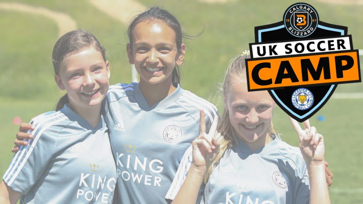 Three young girls in soccer uniforms smiling and posing on a soccer field, with a logo overlay that reads "UK Soccer Camp" and features logos for Calgary Blizzard Soccer and Leicester City Football Club.