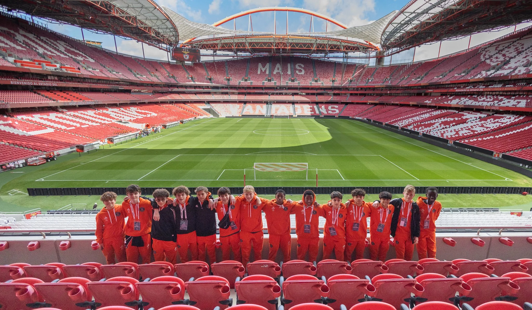 A soccer stadium with empty seats and a group of young soccer players in orange uniforms standing in front of the field.