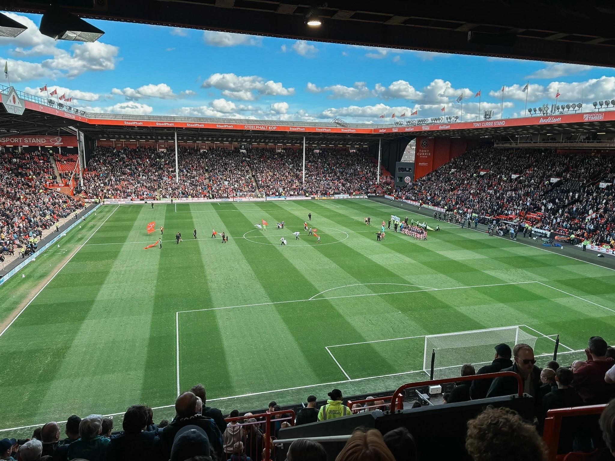 A soccer stadium filled with spectators before a match, with players warming up on the field.