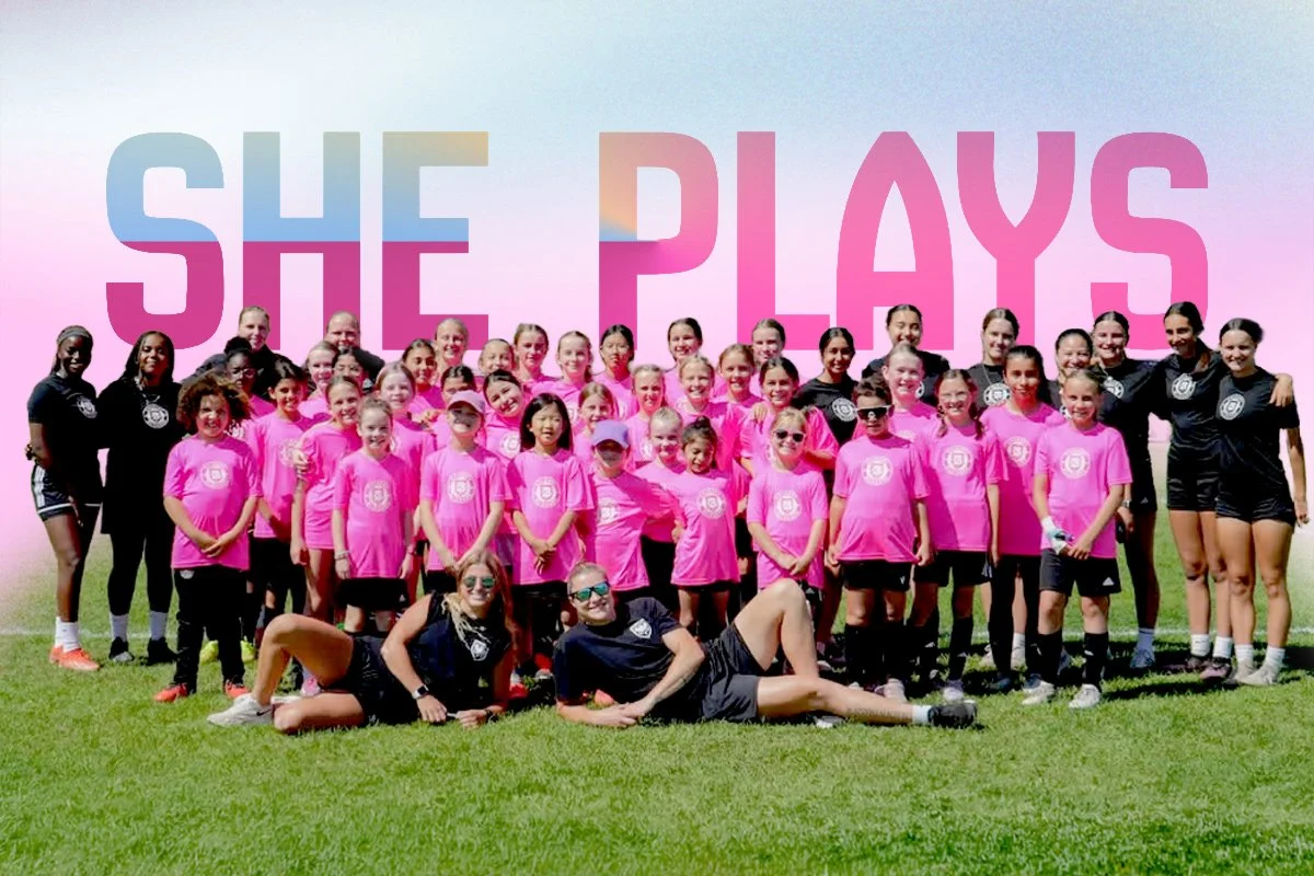 A group of young girls and women in pink and black athletic uniforms posing outdoors on a grassy field for a photo, with a large text background promoting Blizzard Calgary, an all girls camp in July 2026, and a logo at the top.