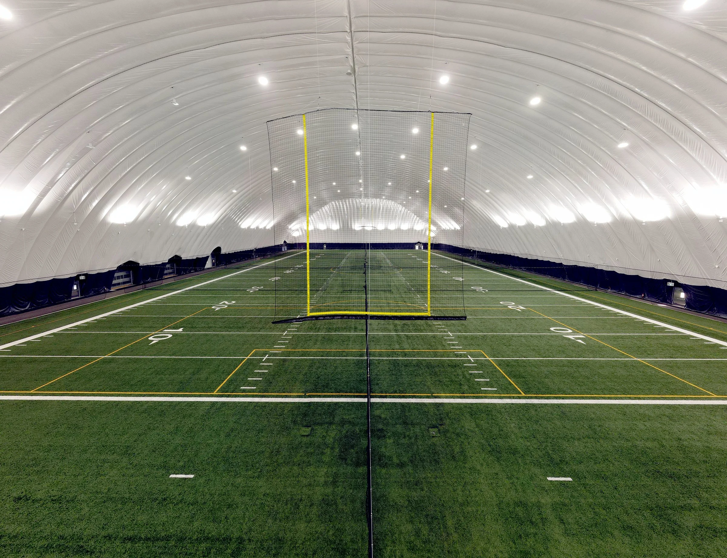 Indoor football field inside a large, white, dome-shaped facility with artificial turf and painted yard lines.