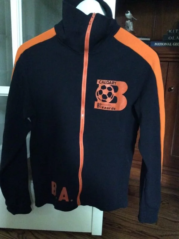 Black jacket with orange accents, featuring a Calgary Blizzard logo with a soccer ball, and the letters B A on the lower front.