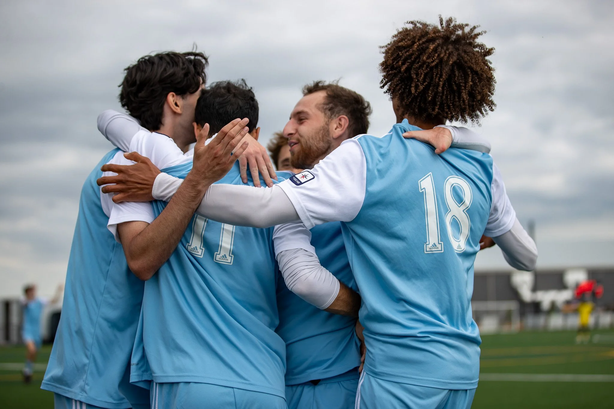 Group of soccer players in light blue jerseys hugging each other on the field