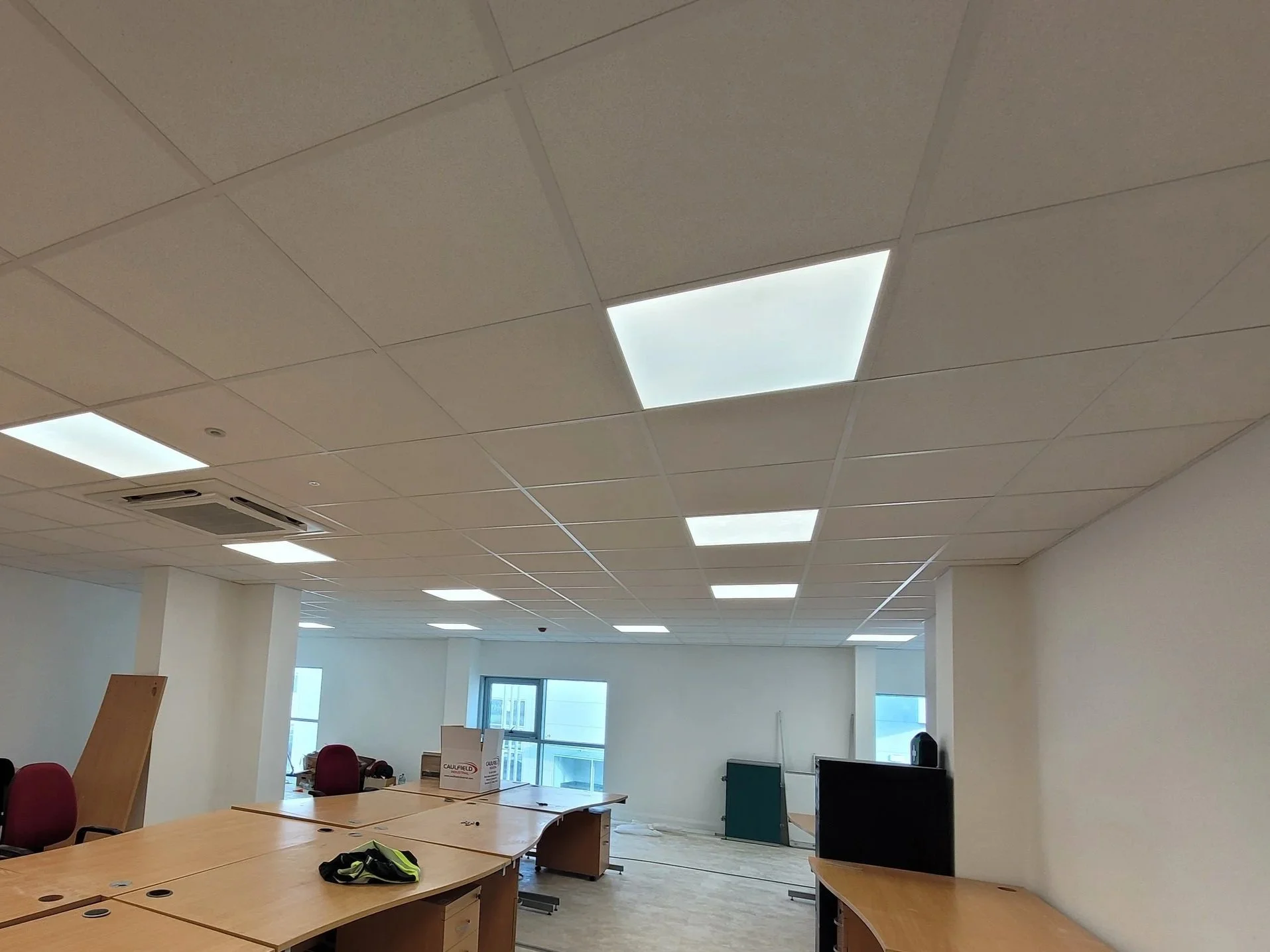 Construction site of an interior space showing ongoing work on partitions, ceiling, and framing with exposed metal studs, electrical wiring, and new windows.
