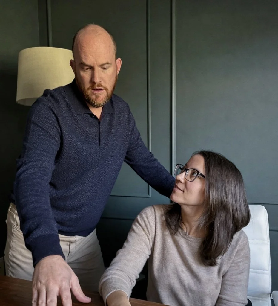A man with a beard and a woman with glasses having a serious conversation in an office.