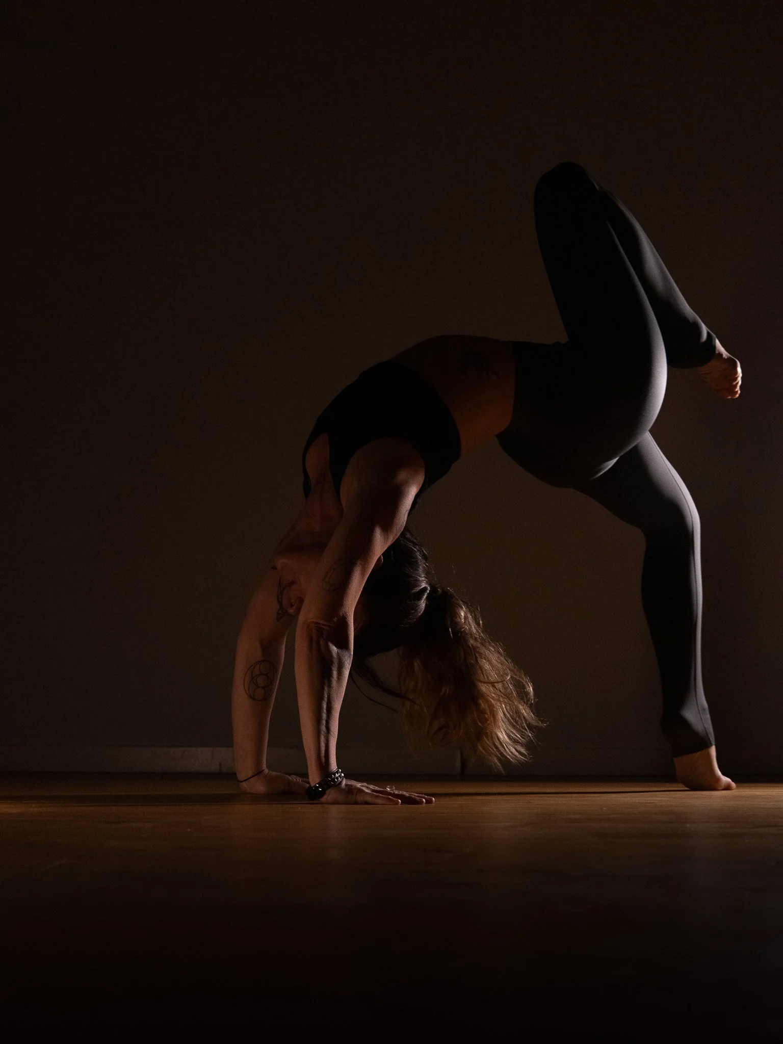 A woman practicing yoga in a dimly lit room, performing a handstand with her legs extended upward and her body arched.