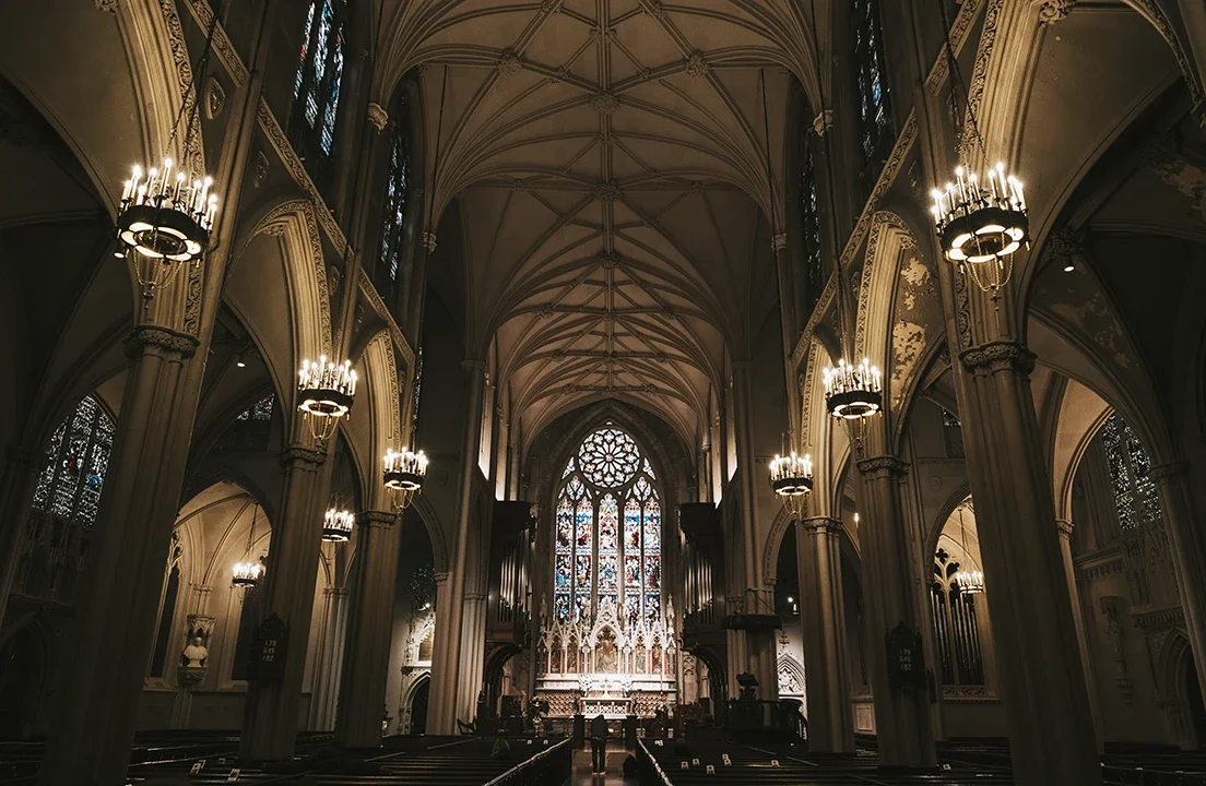 Dan Kyzer, Classical Guitar | Pictured is an interior of a Gothic-style church with high vaulted ceilings, stained glass windows, and ornate chandeliers.