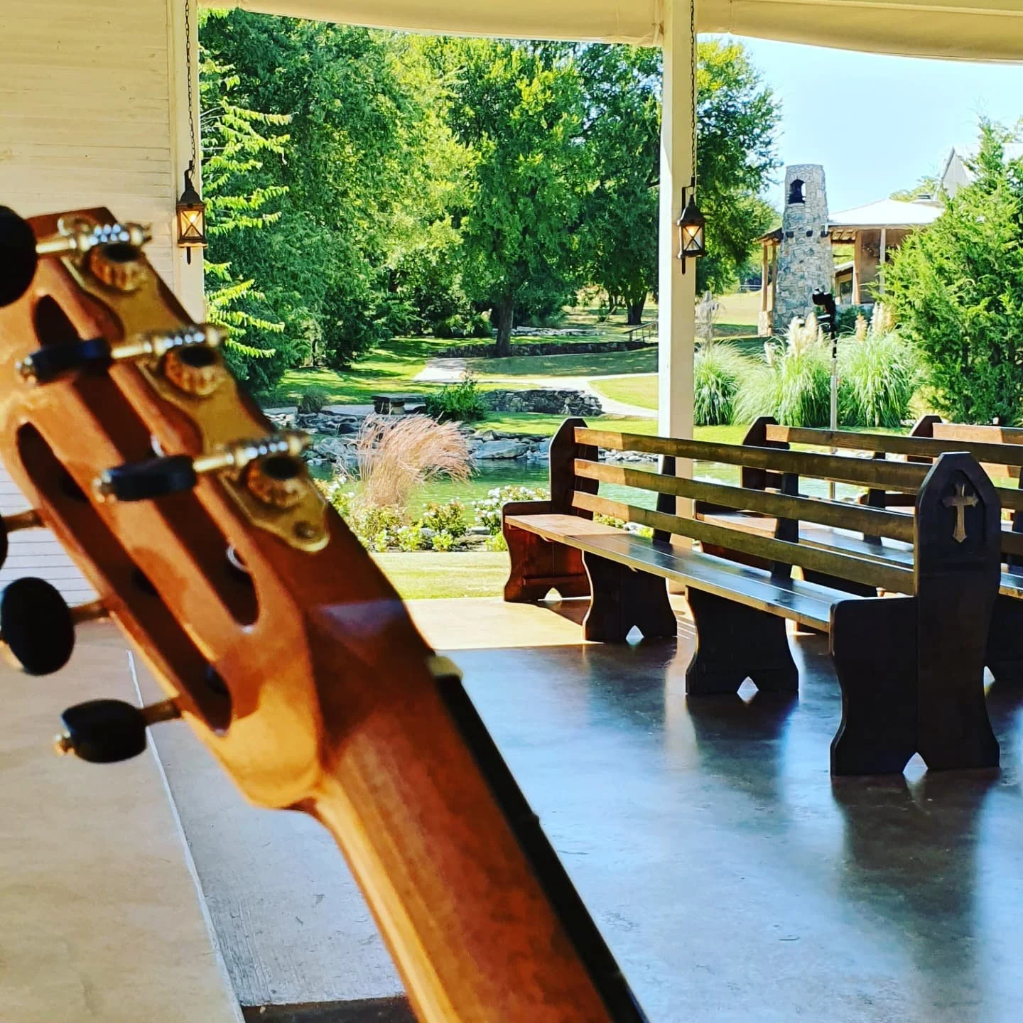 Dan Kyzer, Classical Guitar | Pictured is Dan's guitar neck in the foreground with a park view including trees, benches, and a stone fireplace in the background.