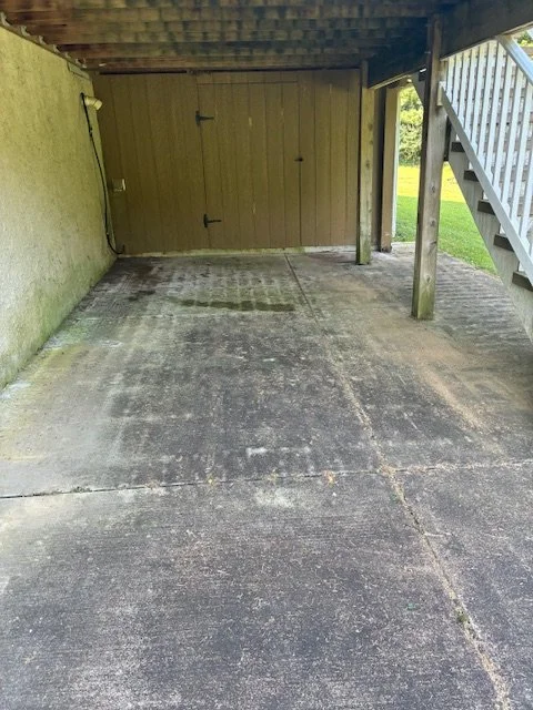 Empty concrete carport with a wooden staircase and a closed double barn door at the back