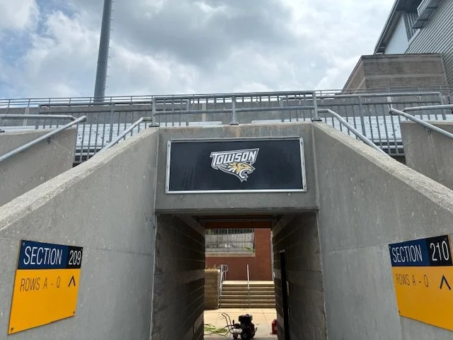 Entrance to a sports stadium tunnel with a Towson University logo and signs indicating sections 209 and 210.