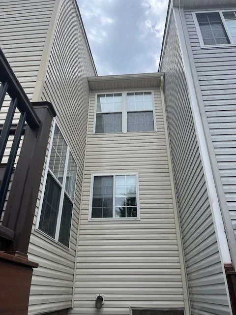 View of three-story beige siding house from the ground, looking up, with windows and a cloudy sky.