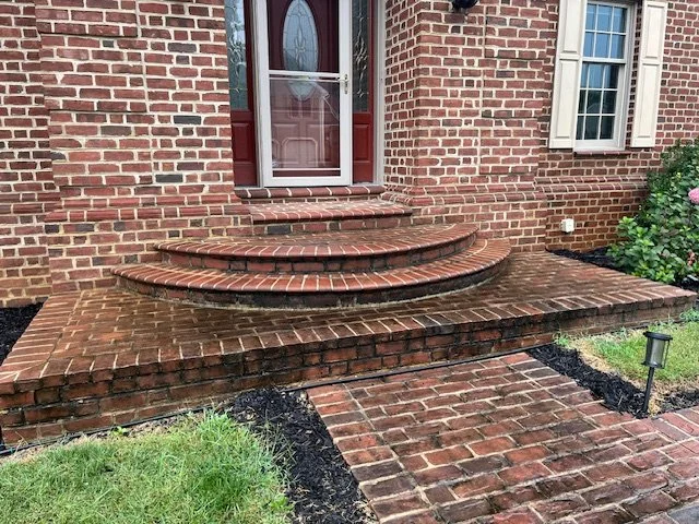 Brick steps and walkway leading to a house entrance with a door and window, surrounded by a garden.