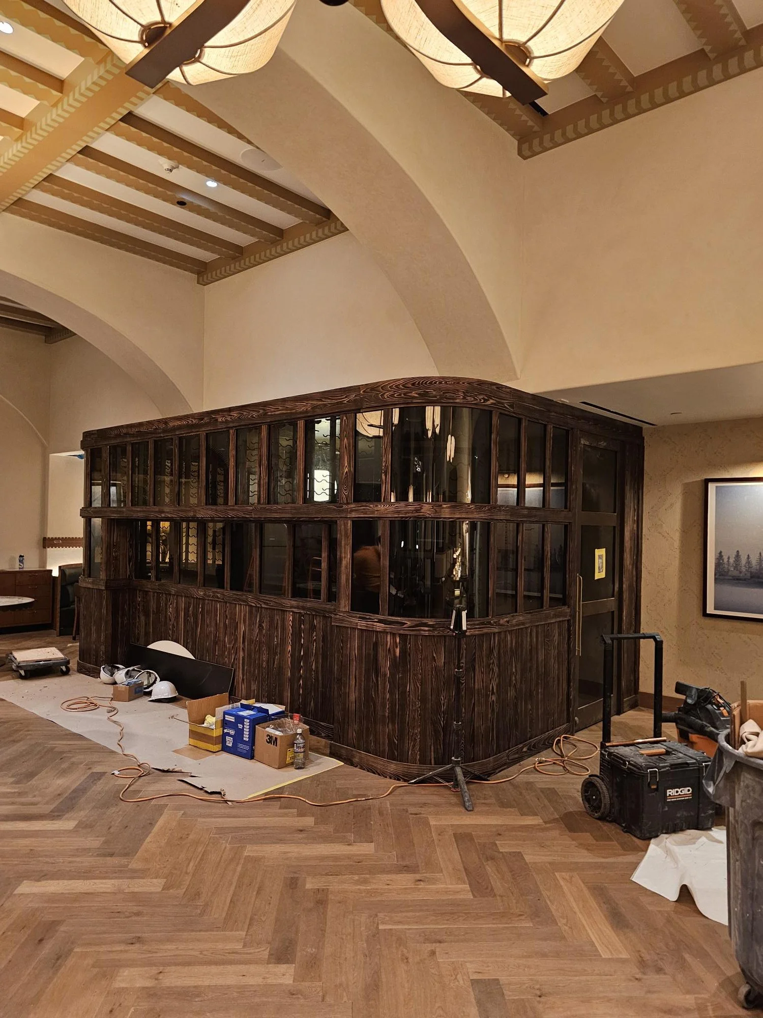 A wooden corner structure with glass panels in a room under renovation, with construction tools and supplies on the floor.