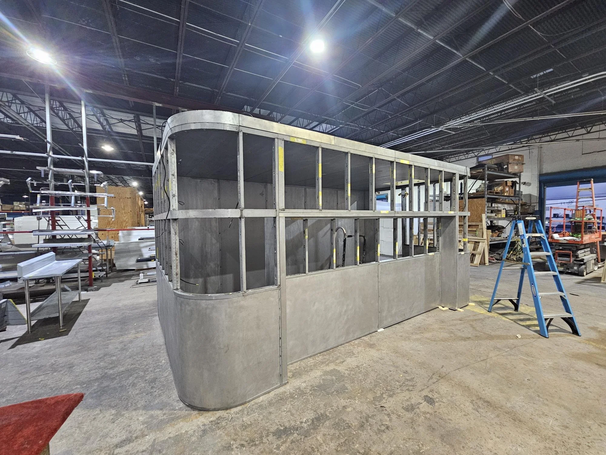 Metal framework for a structure in a workshop or warehouse, surrounded by ladders, shelves, and tools.