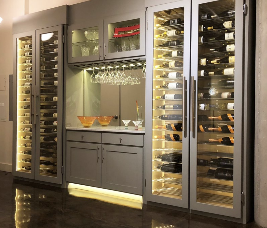 A wine storage cabinet with glass doors, illuminated interior, filled with wine bottles, and a small bar area with glasses and decorative bowls.