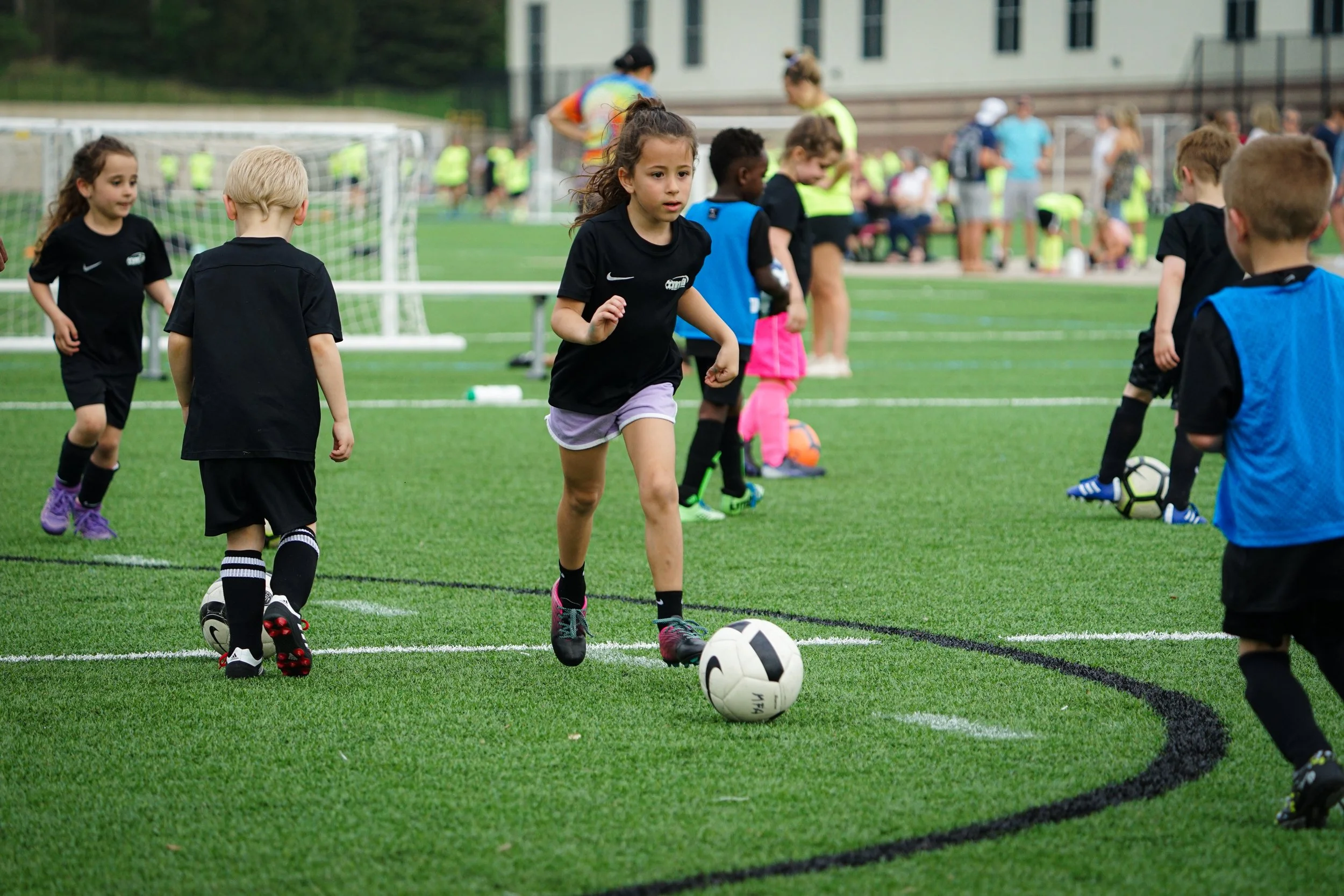 Young soccer players practice dribbling and ball skills during an ACGR Juniors youth soccer training session on a turf field in Grand Rapids, Michigan.