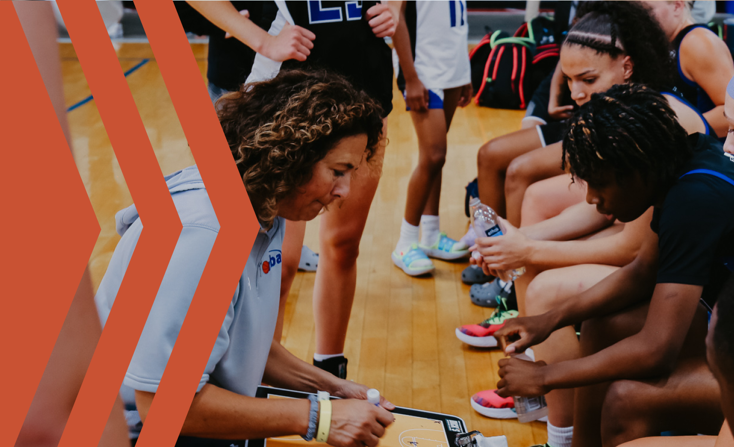 A female coach drawing up a game plan while coaching a girls basketball team during a timeout in a gymnasium.