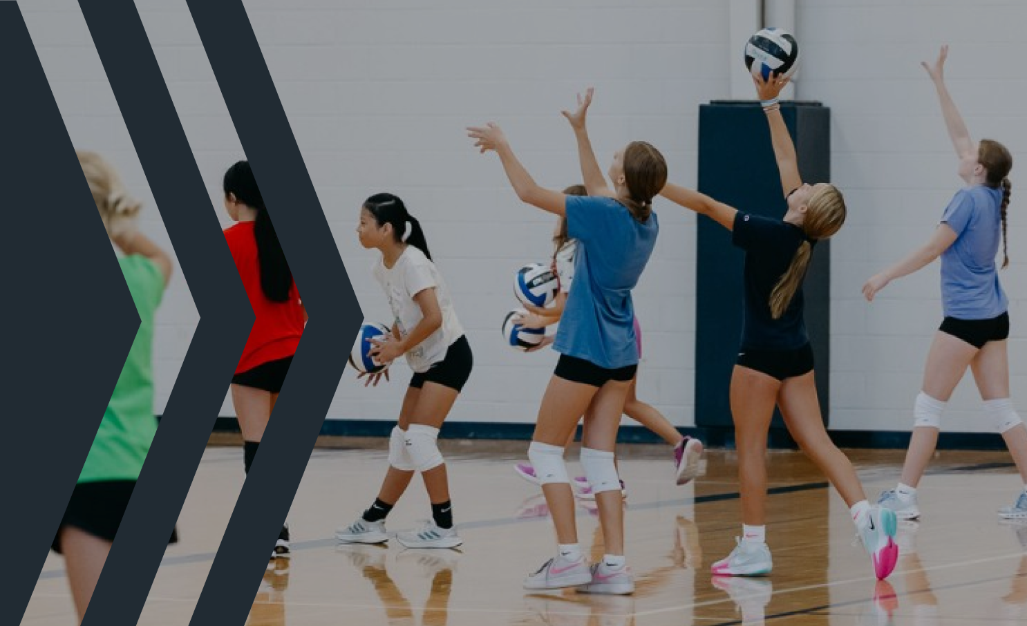 Young girls playing volleyball in a gym, with some preparing to hit or receive the ball.