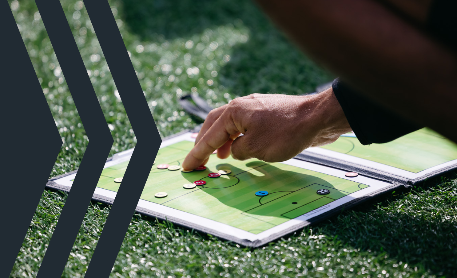 A person's hand with a coach or player on a soccer tactics board on the grass, placing or moving a red token, during soccer strategy planning.