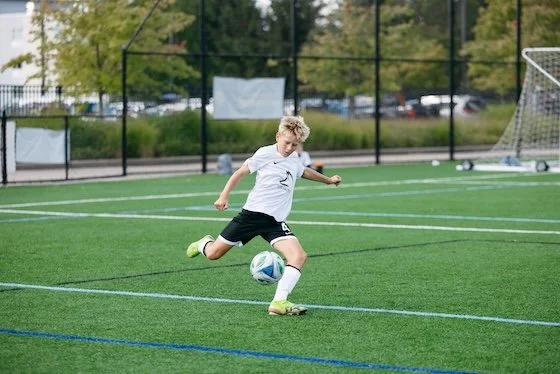 Young boy playing soccer on a green field, kicking a ball.