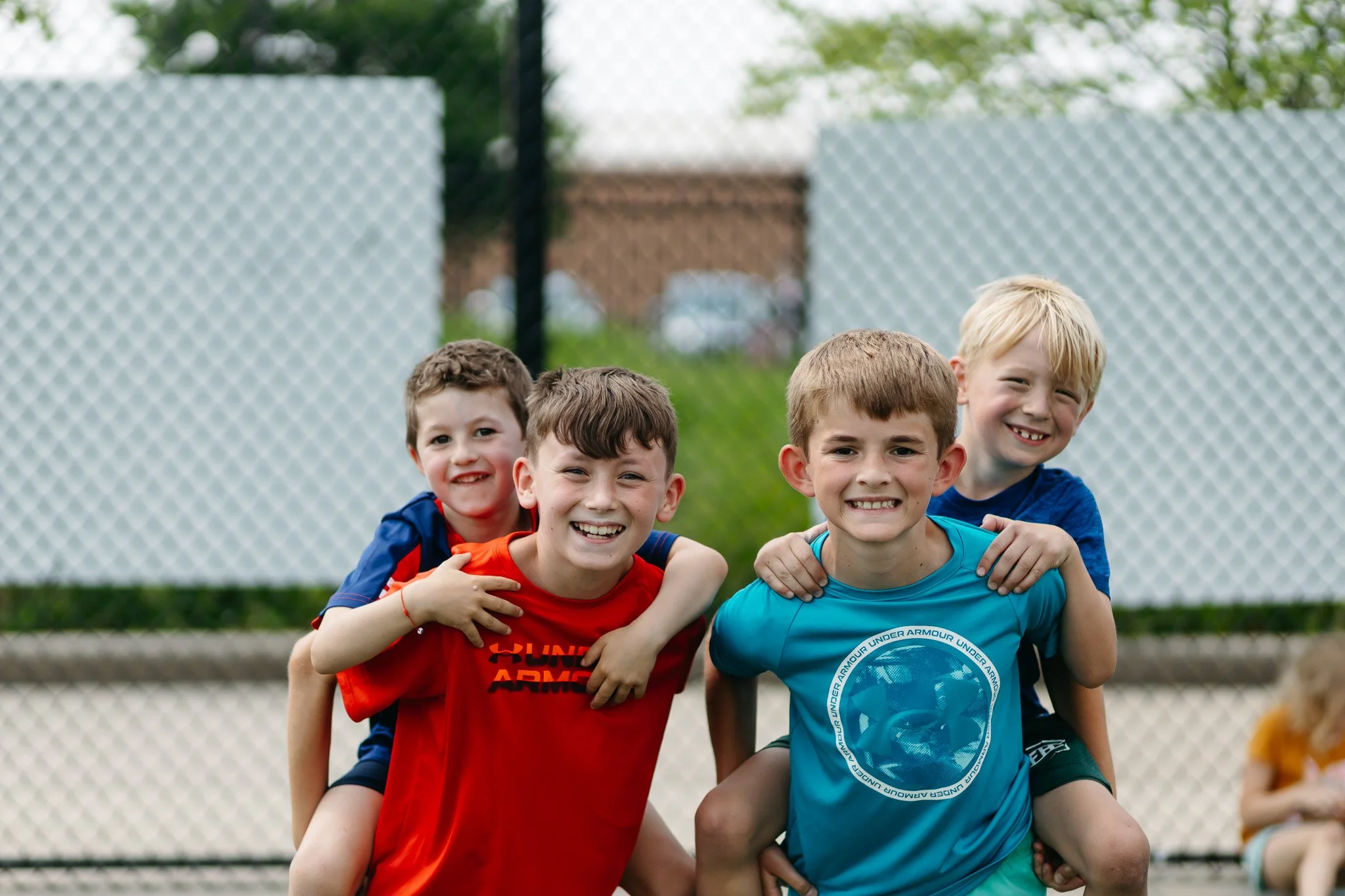 Four campers laugh together while giving piggyback rides during All Day with MSA at Michigan Sports Academies. Kids build friendships, teamwork, and confidence through outdoor summer camp activities and youth sports.