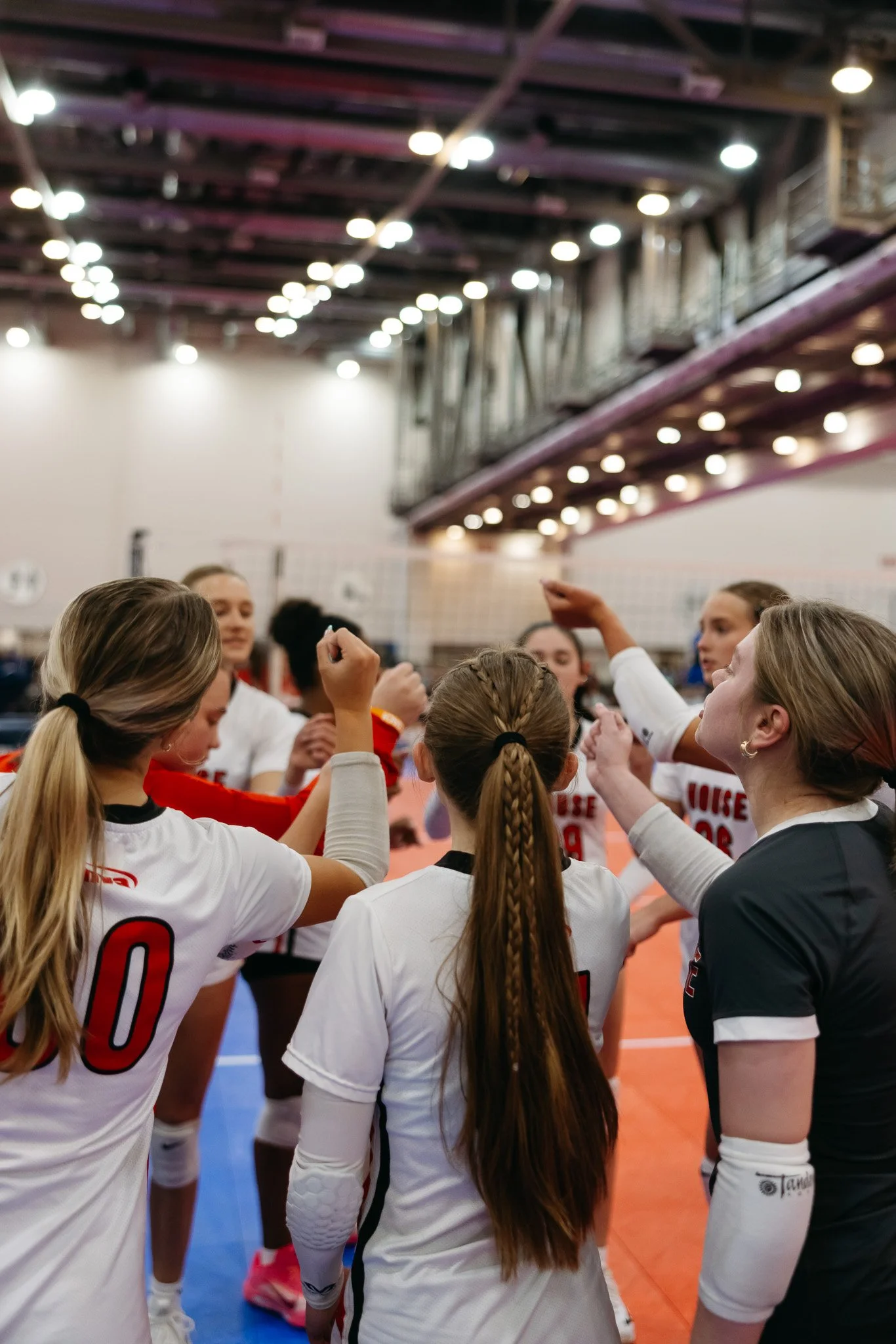 High school volleyball athletes gather in a team huddle before a club season game for MVA raising their hands together.