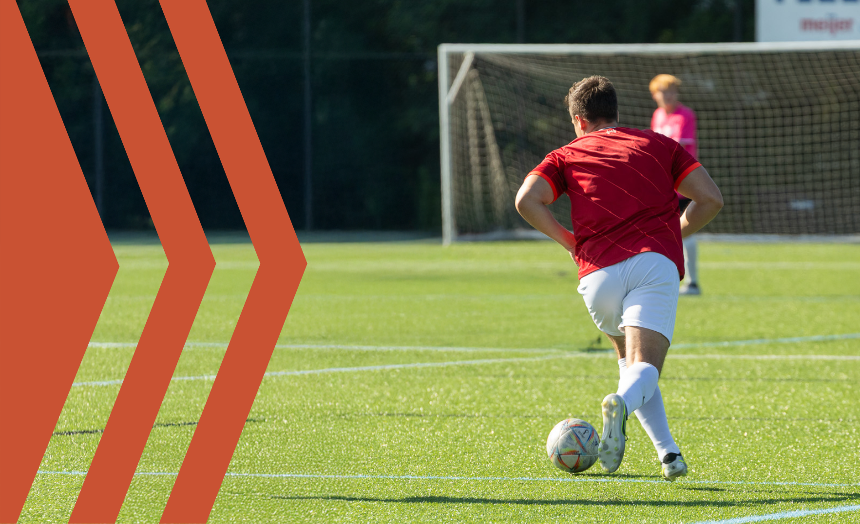 An adult in a red arsenal jersey playing soccer on a turf field in an adult soccer league in west michigan