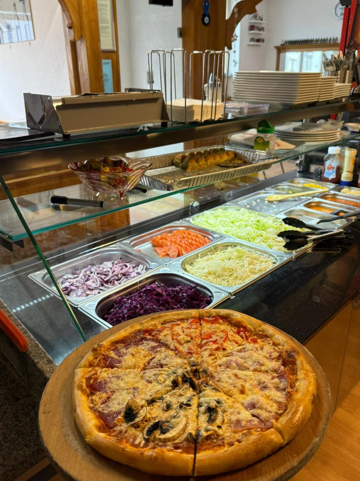 Italienische Pizza vor einer Salatauswahl in einem Selbstbedienungsbuffet.