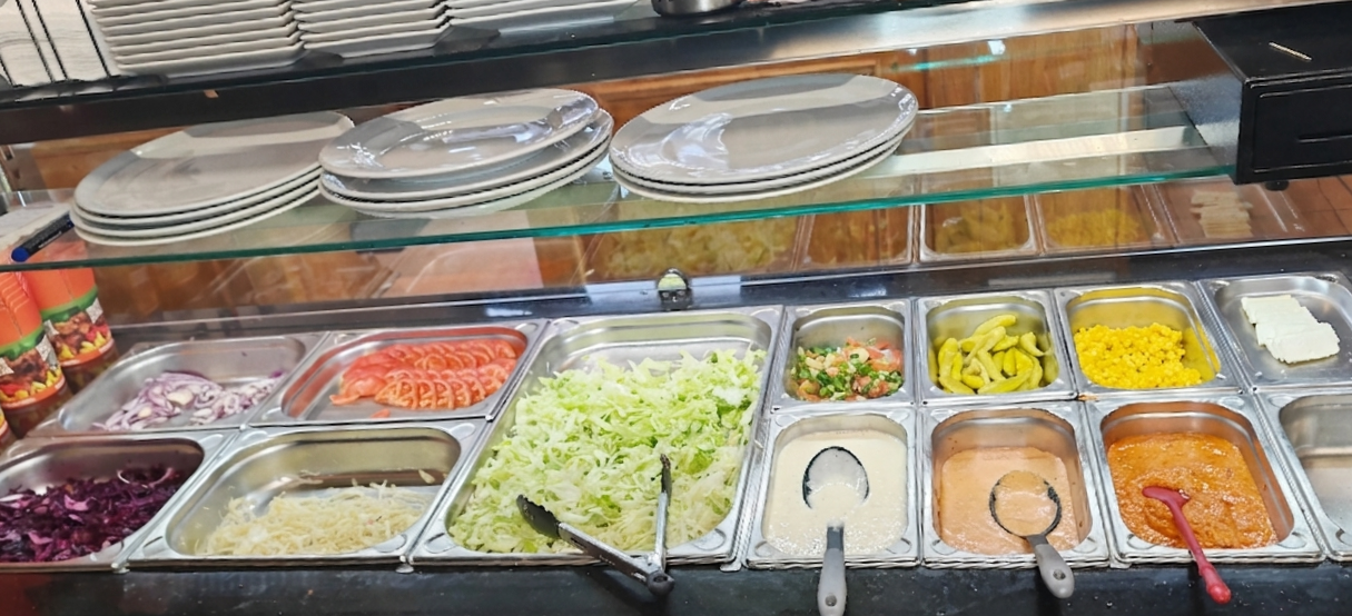 Salat- und Beilagenbuffet mit frischem Salat, Tomaten, Zwiebeln, Sauerkraut, Lachs, verschiedene Saucen, eingelegtem Gemüse und andere Zutaten.